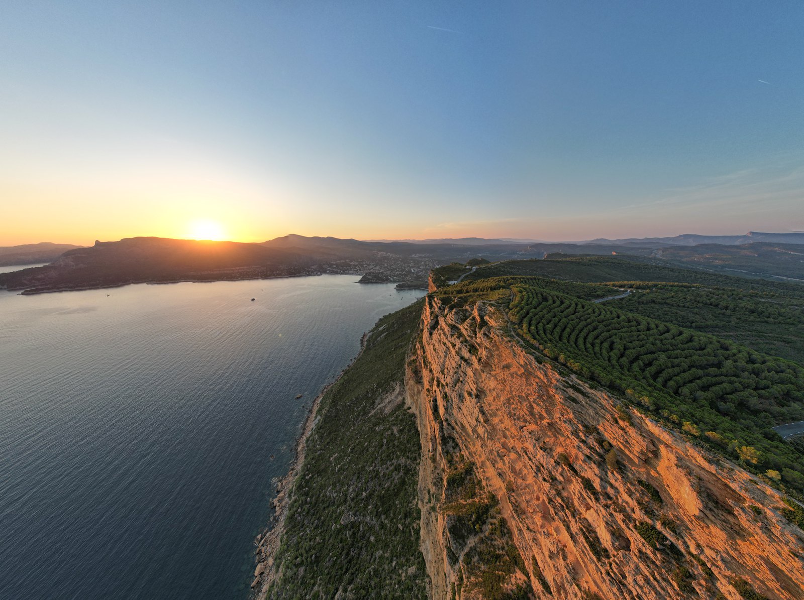 Sun setting over the sea beside a long red cliff ridge