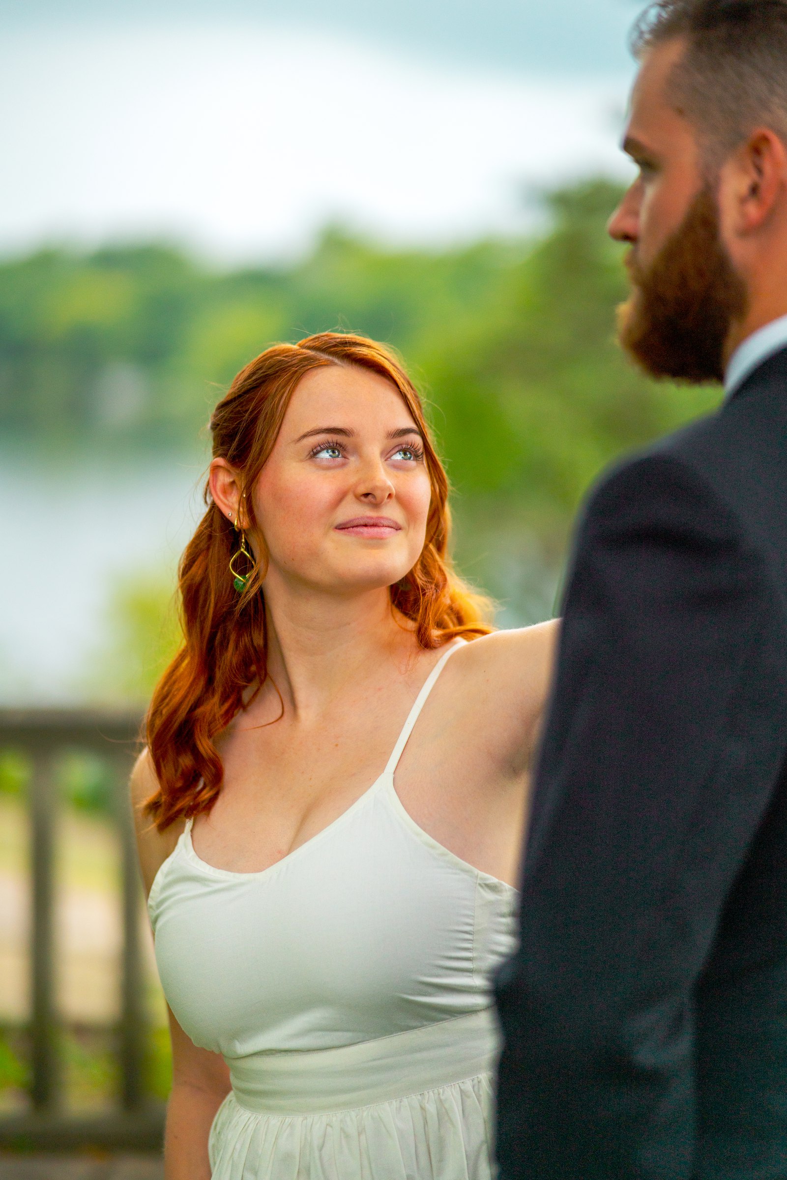 The bride, red hair down, looking up at the groom by a lake