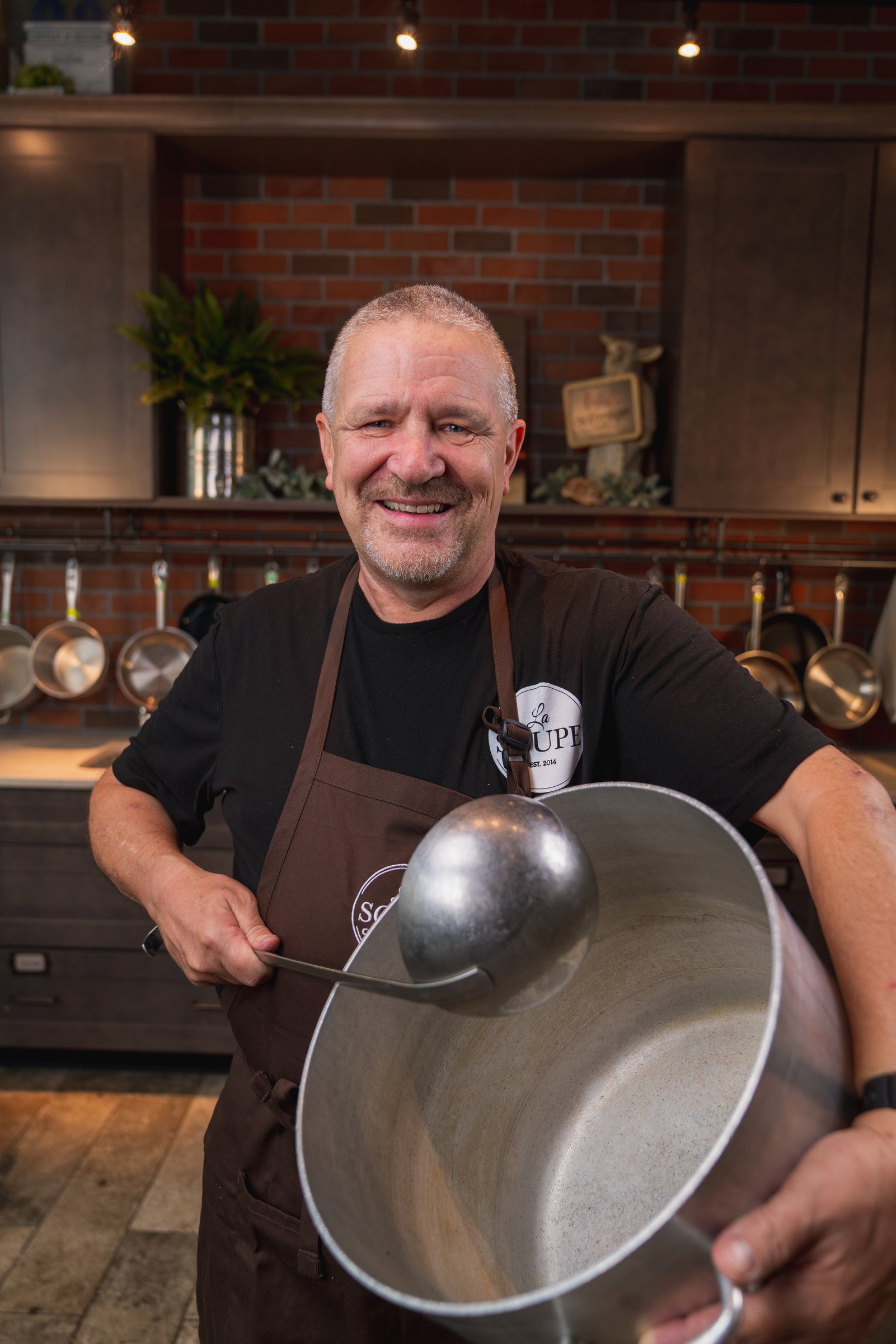 Chef in a brown apron holding a giant ladle and stockpot