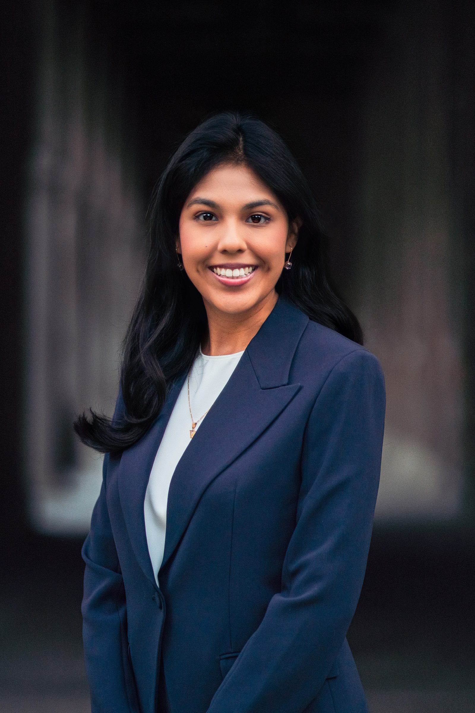 Woman in a navy blazer smiling against a dark background