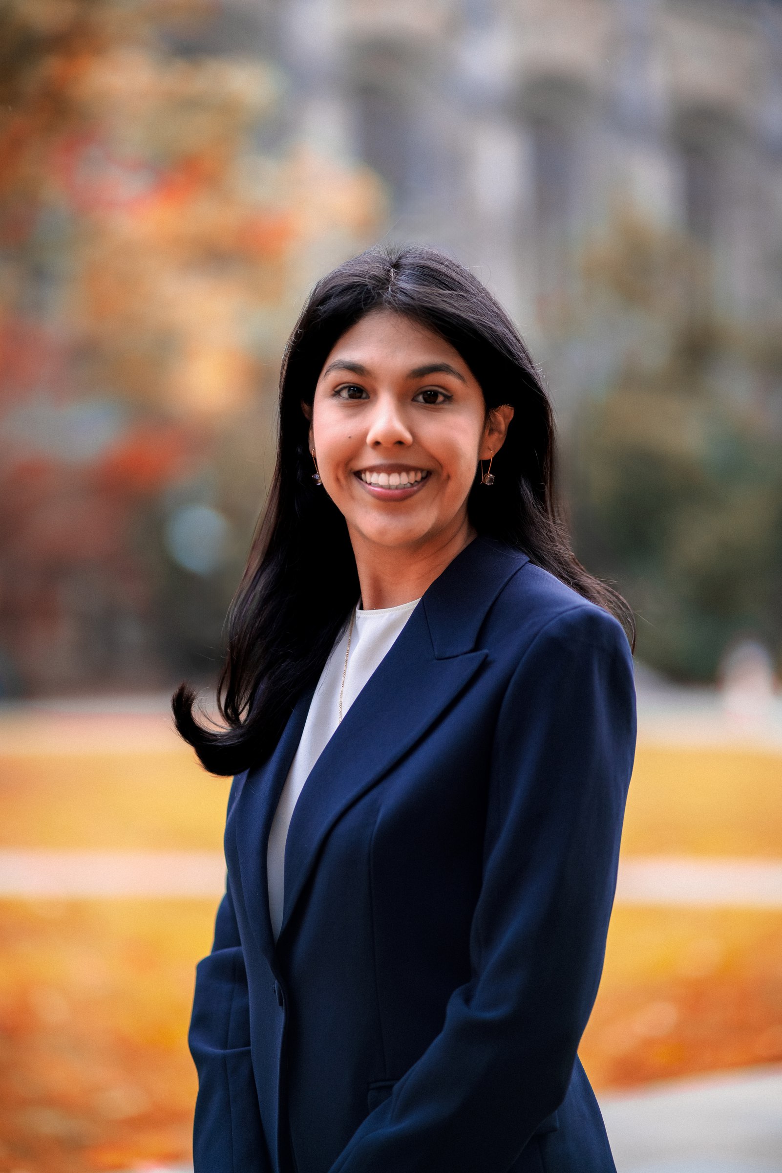 Woman in a navy suit with autumn leaves behind her