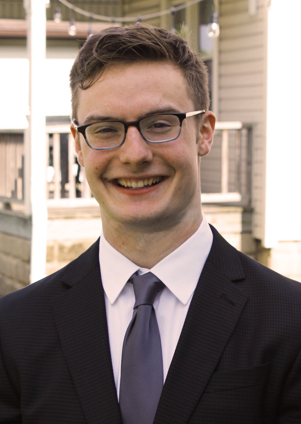 Isaac in 2019, smiling in a suit and glasses