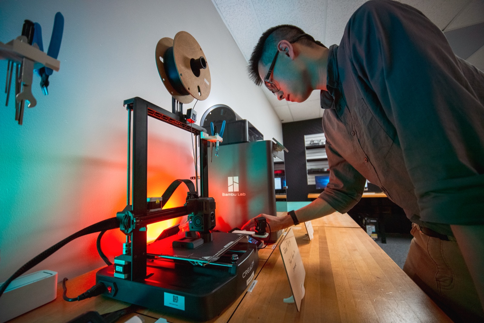 Maker adjusting a 3D printer lit in red and teal