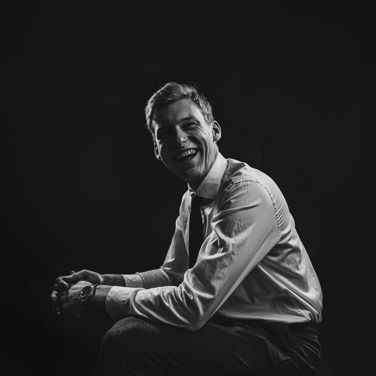 Black and white studio portrait of a laughing man in a shirt and tie
