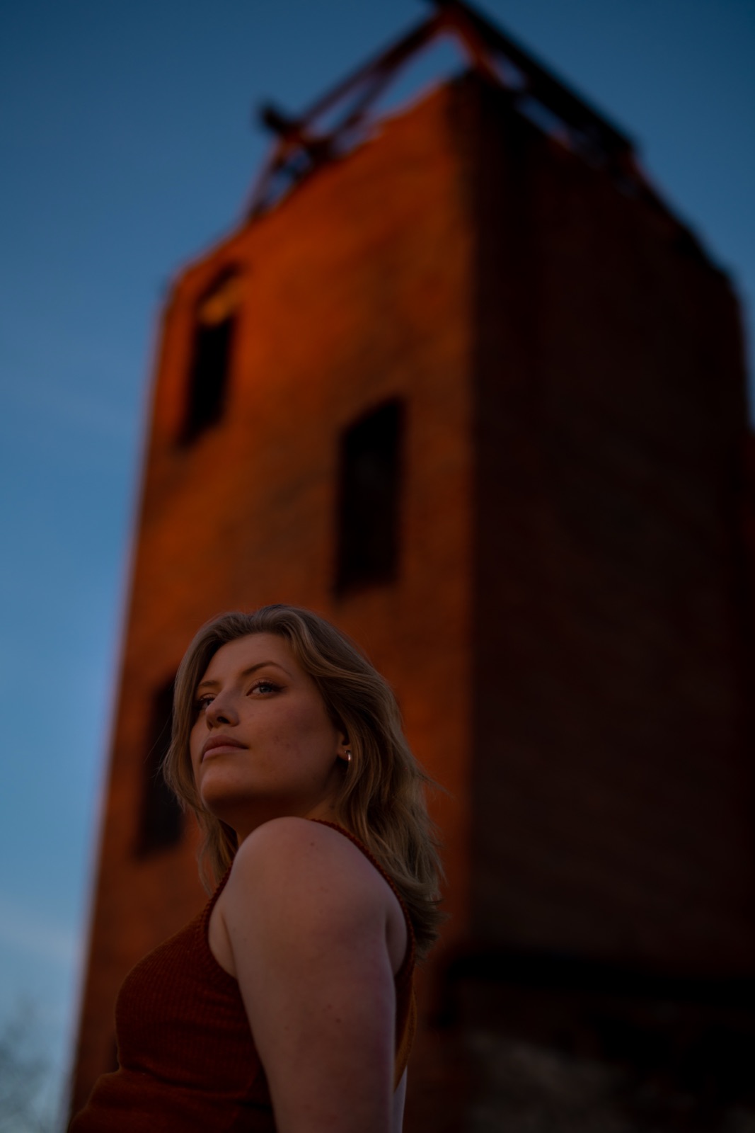 Woman looking up beside an old brick tower at dusk