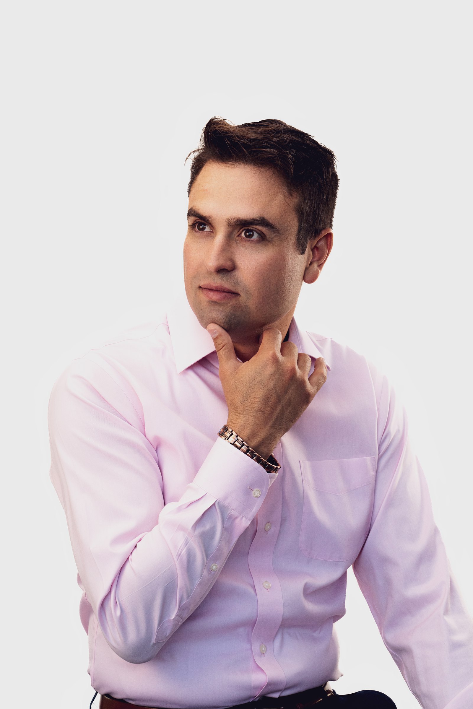 Man in a pink shirt, hand at his chin, on white