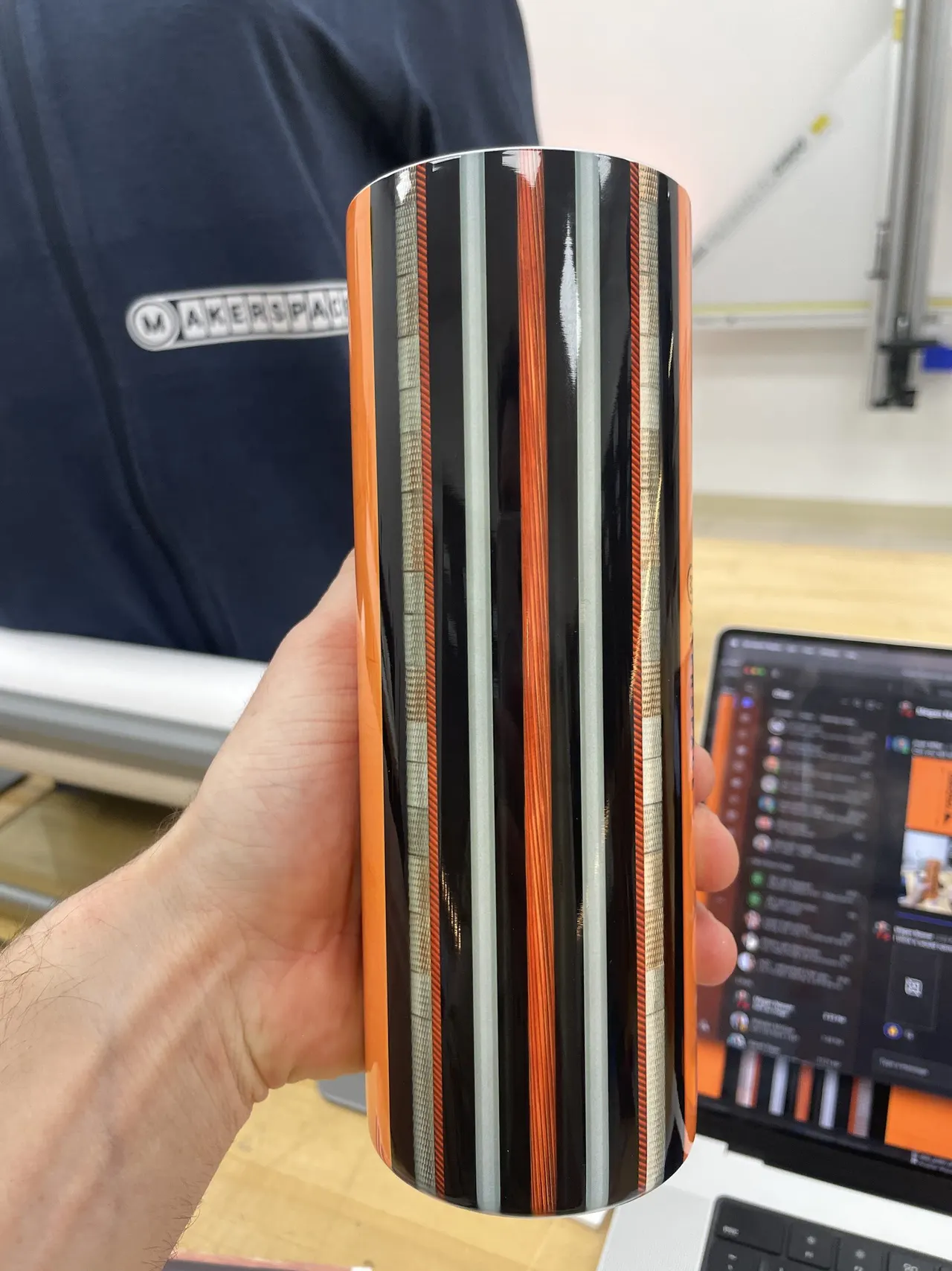 A tall tumbler striped in orange, black and white, held up in the Makerspace