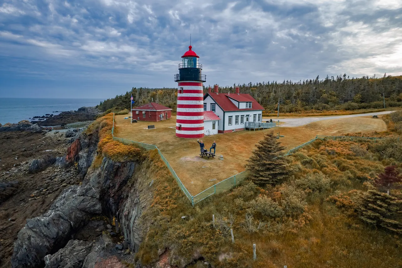 A red and white striped lighthouse on a green headland above rocky shore