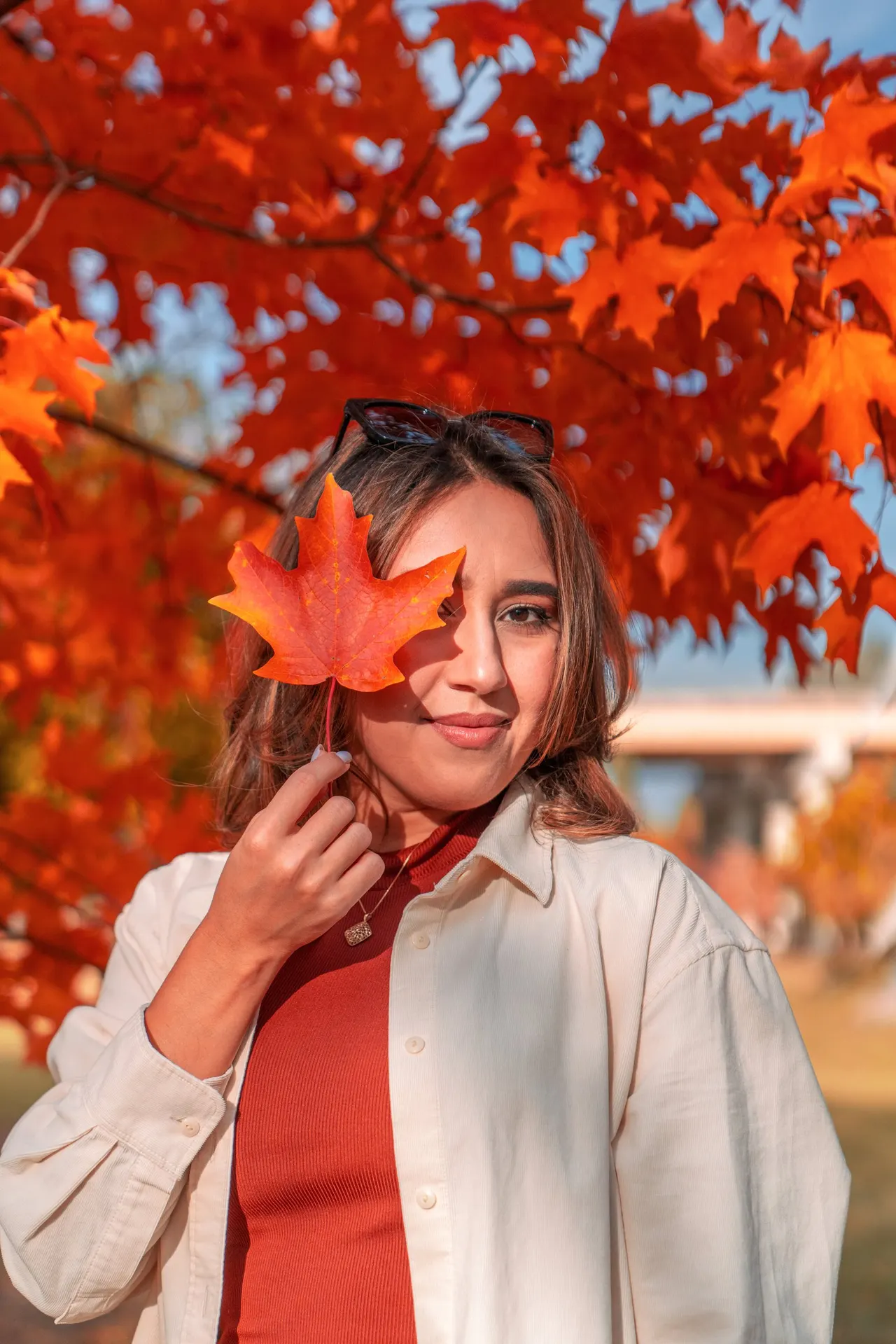 A woman holding a red maple leaf over one eye