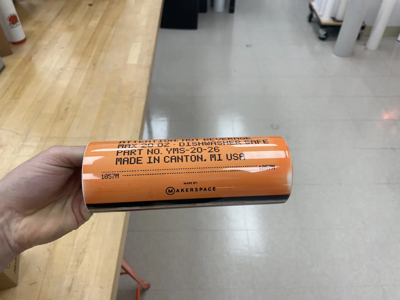 The orange back of a tumbler printed with a part number, MADE IN CANTON, MI USA and the Makerspace logo