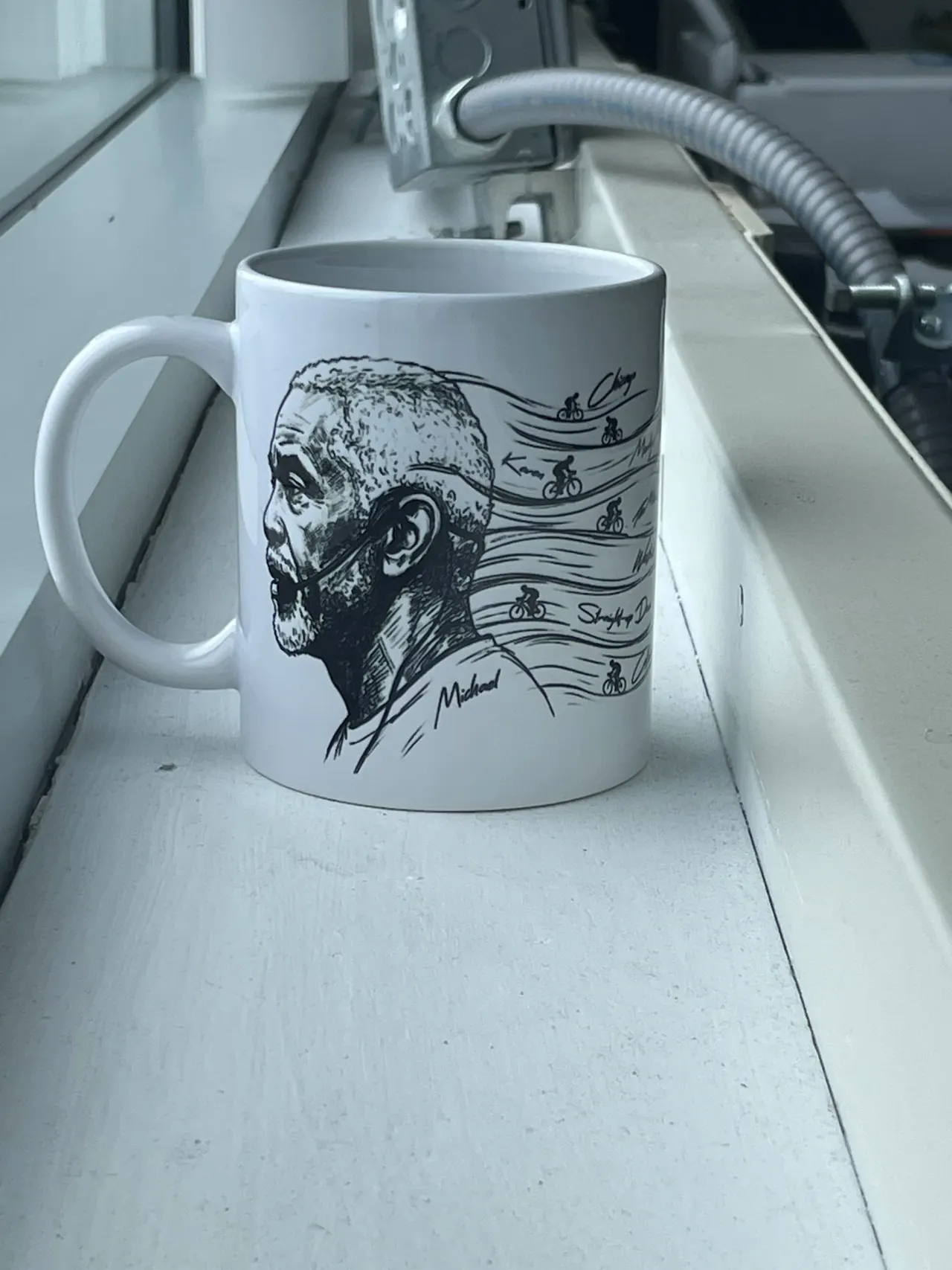 A white mug with a black line portrait of a coach, cyclists riding across the waves behind him