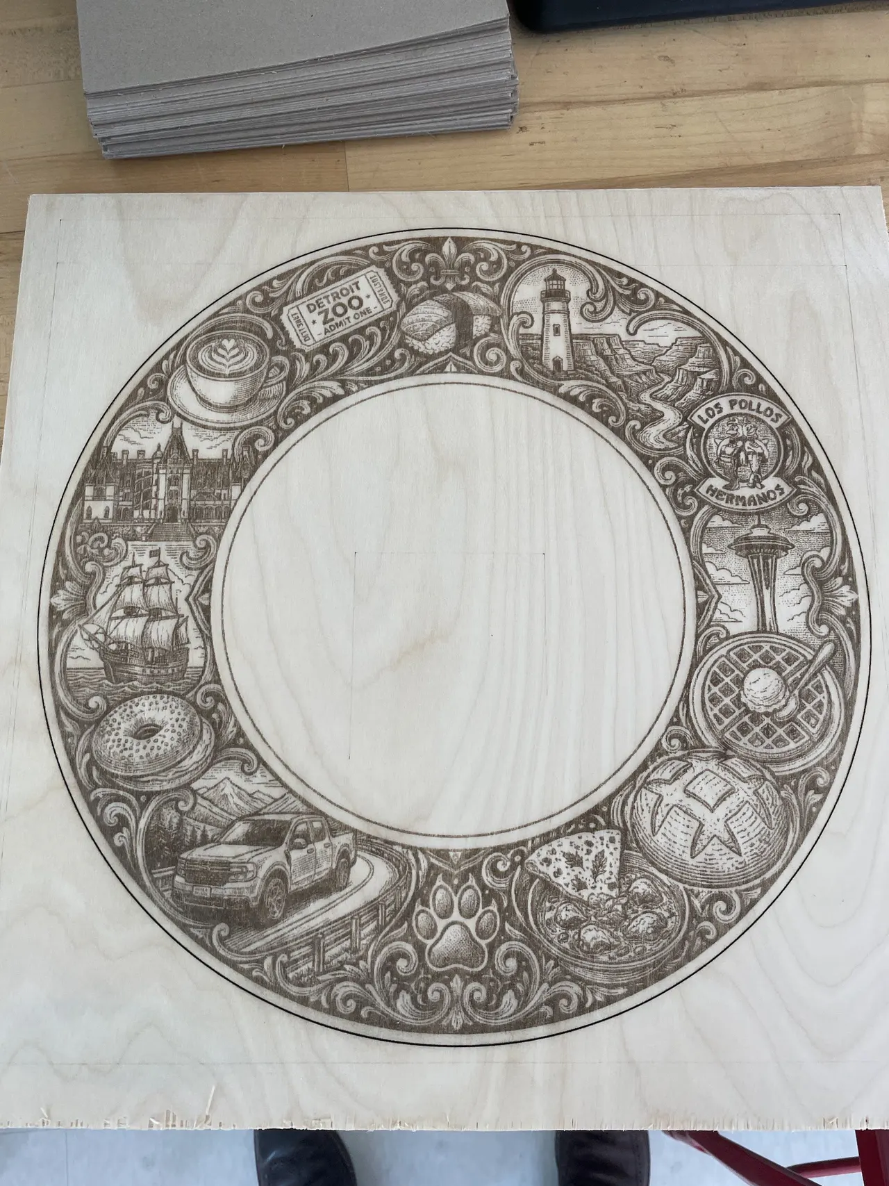 A ring of engraved scenes on a square of light plywood
