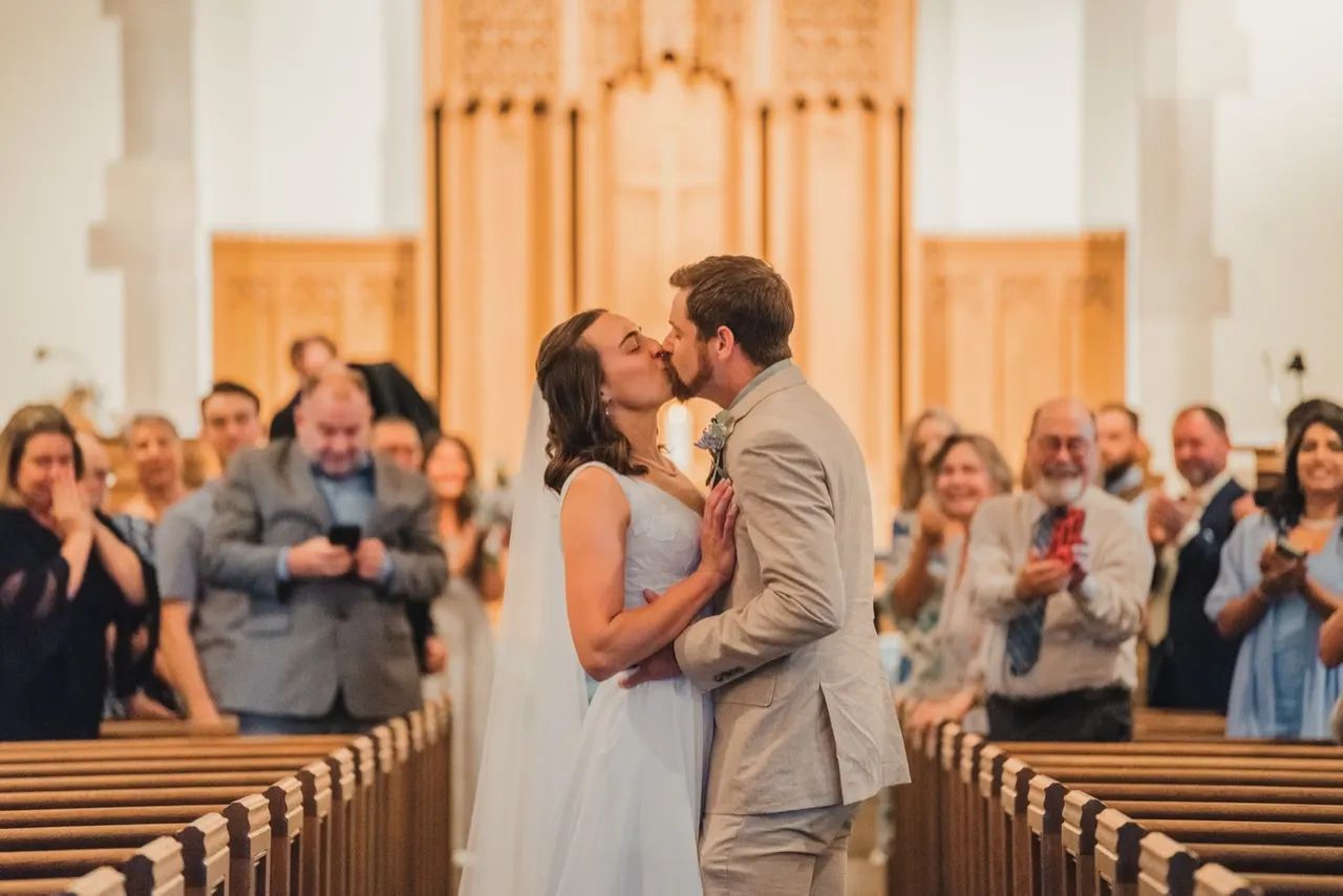 Couple kissing in the church aisle as guests cheer