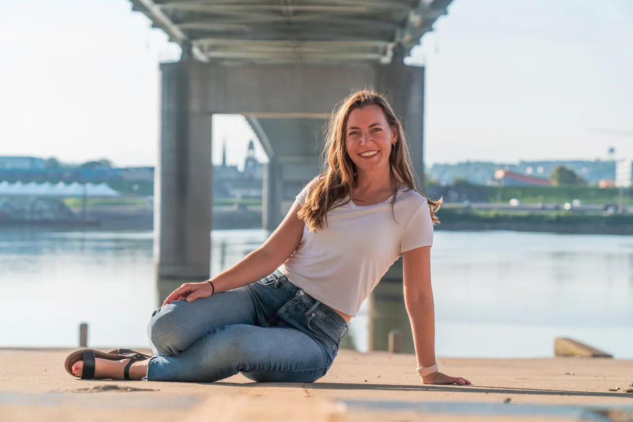 A woman sitting on the riverbank beneath a bridge