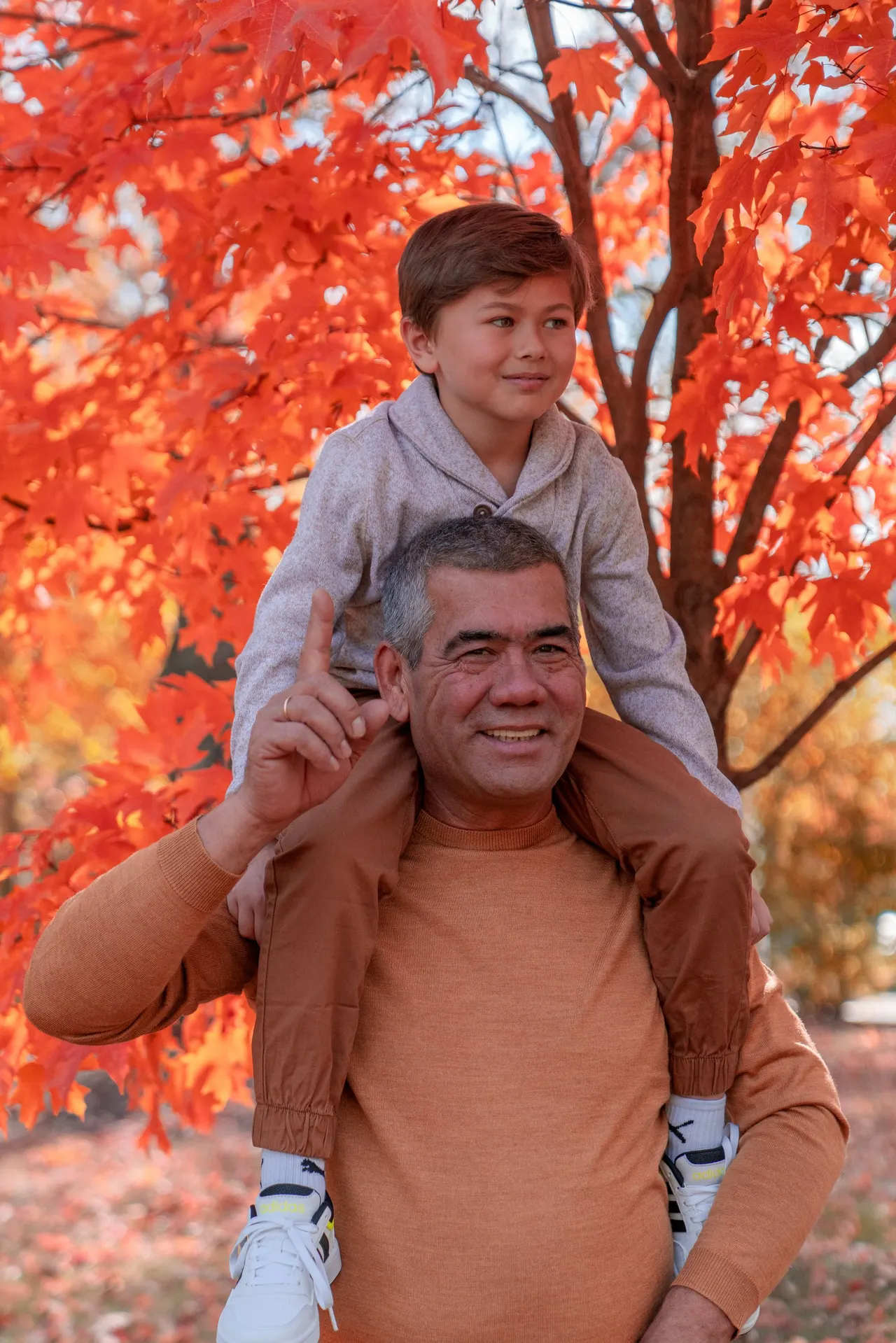 A boy riding on a man's shoulders under a red tree