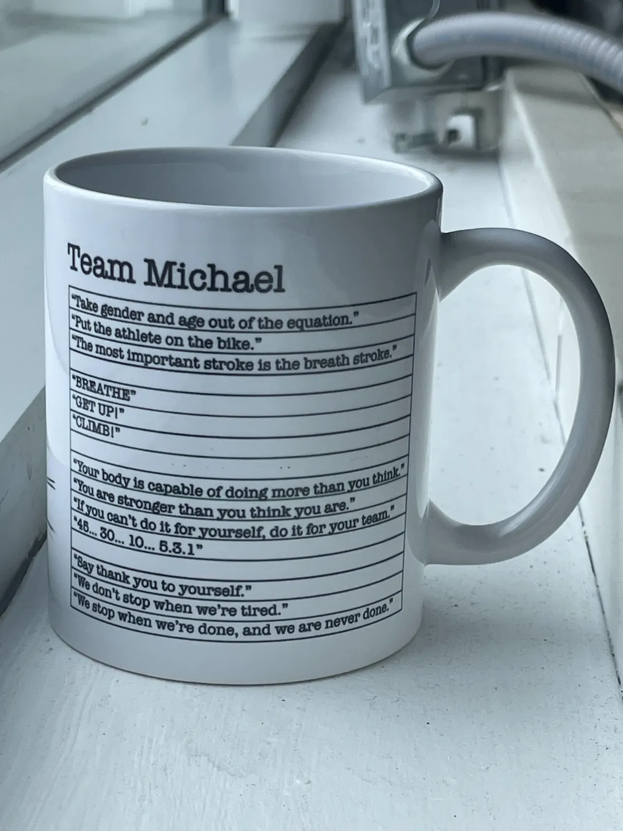 A white mug printed with a list of quotes from a cycling coach
