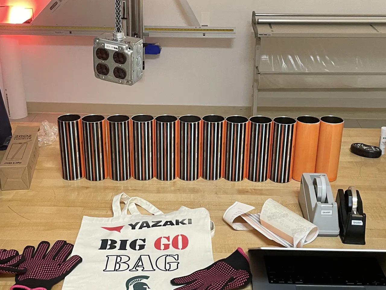 Striped and orange tumblers lined up on a bench in the Makerspace