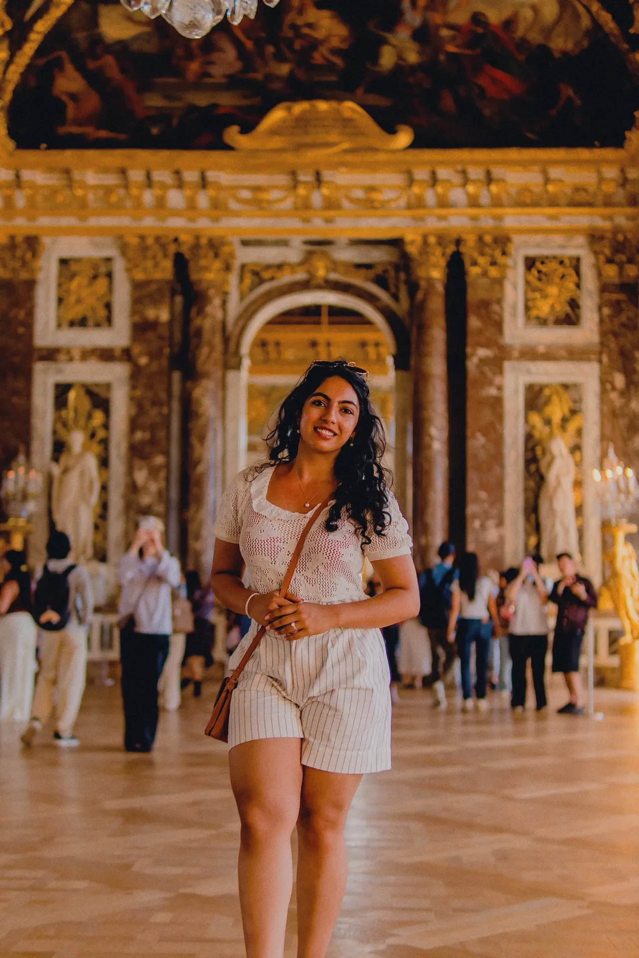 A woman walking through a gilded hall at Versailles