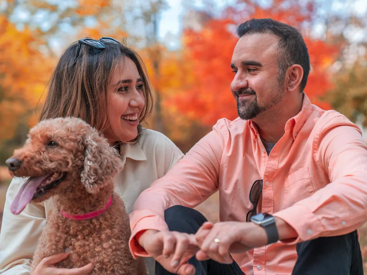 A couple laughing with their curly-haired dog in the leaves