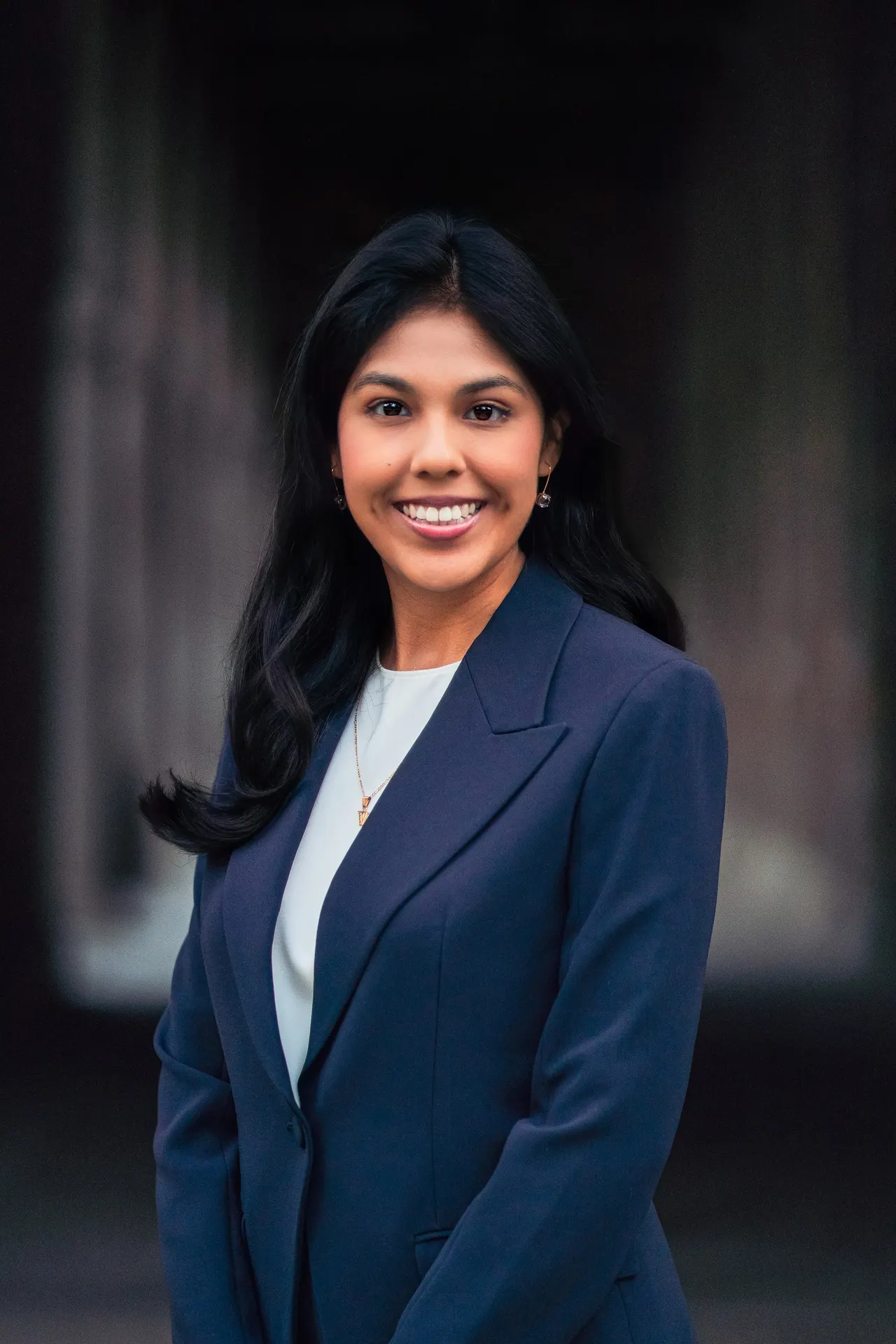 Woman in a navy blazer smiling against a dark background