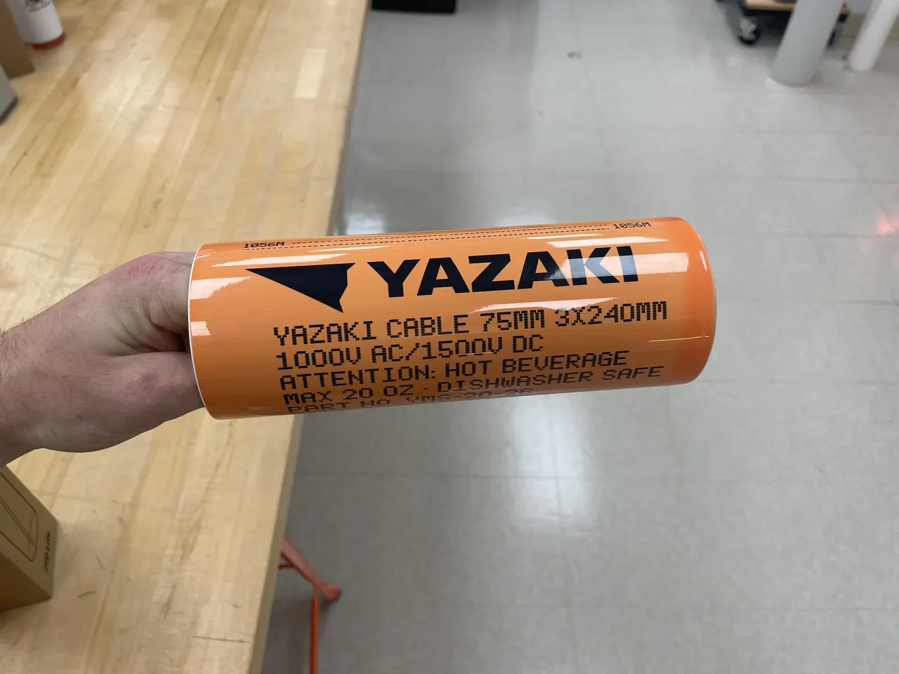 An orange tumbler printed with the Yazaki logo and cable markings, held sideways