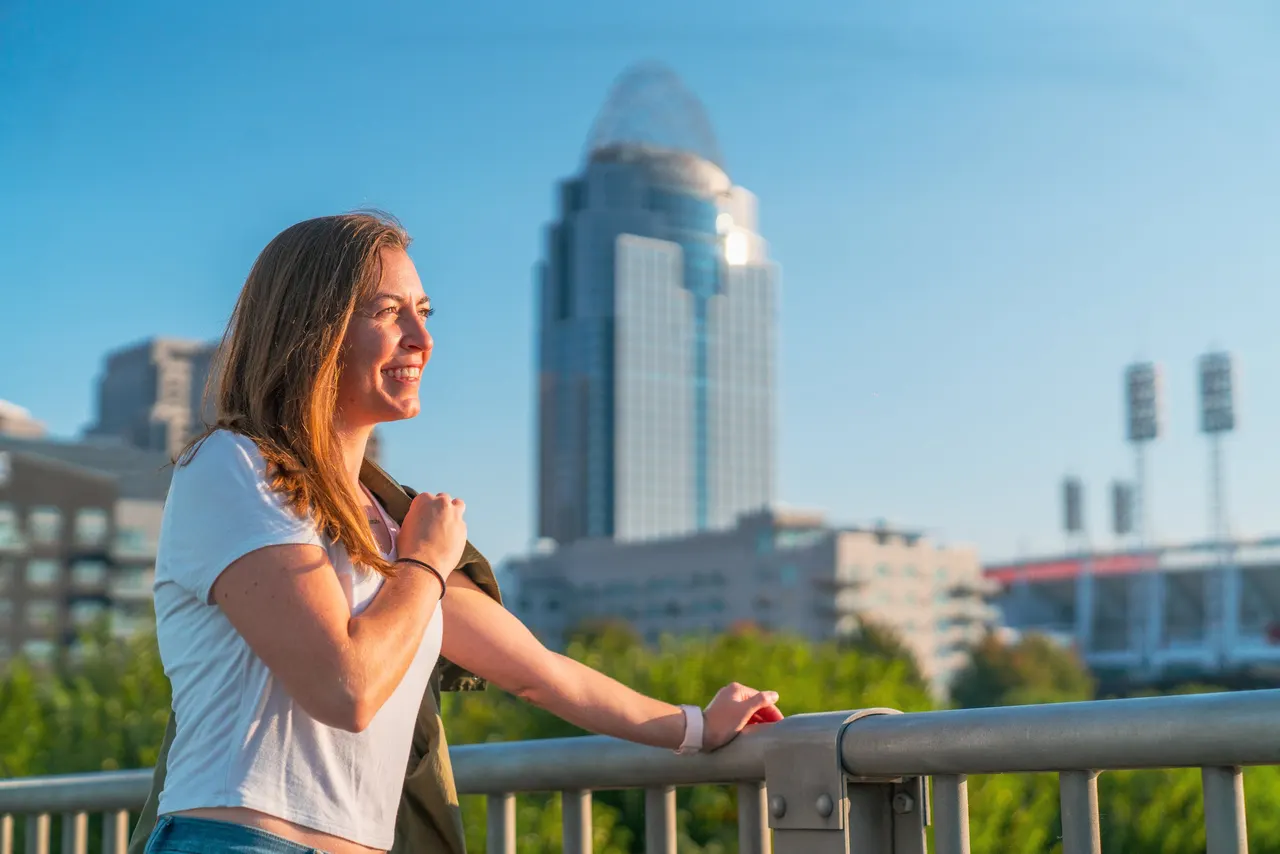 A woman leaning on a railing, the Cincinnati skyline behind her