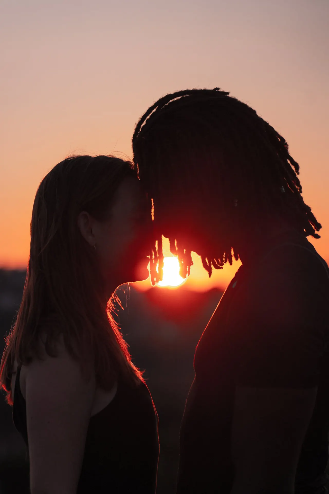 A couple about to kiss, the setting sun between them