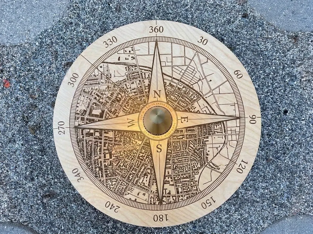 A round light-wood topper engraved with a compass rose over a street map, sitting on a gravel fire pit